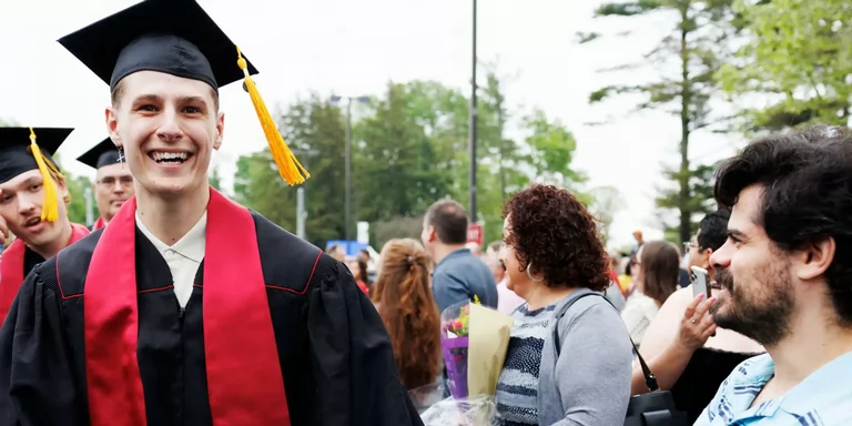 A man in a commencement cap and gown walks through a crowd.