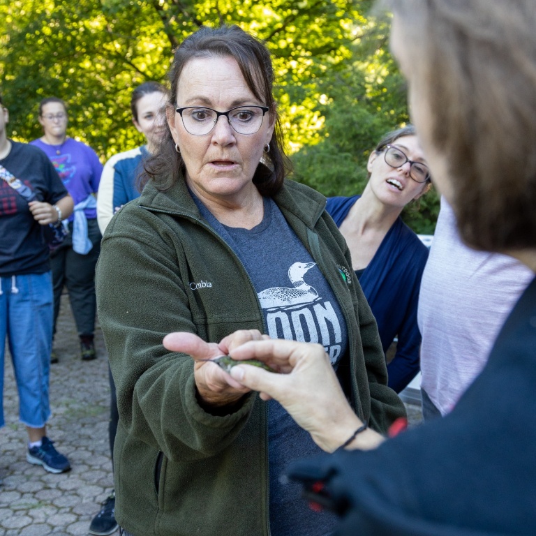 A lady looking astonished at a bird placed on her hand.