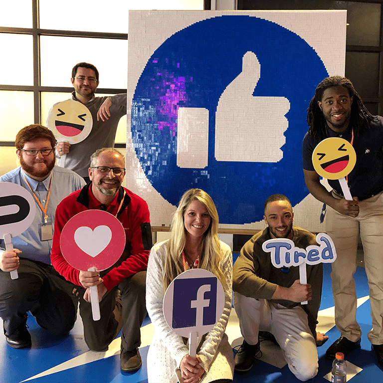 Students and staff standing in front of a Facebook icon and holding signs.