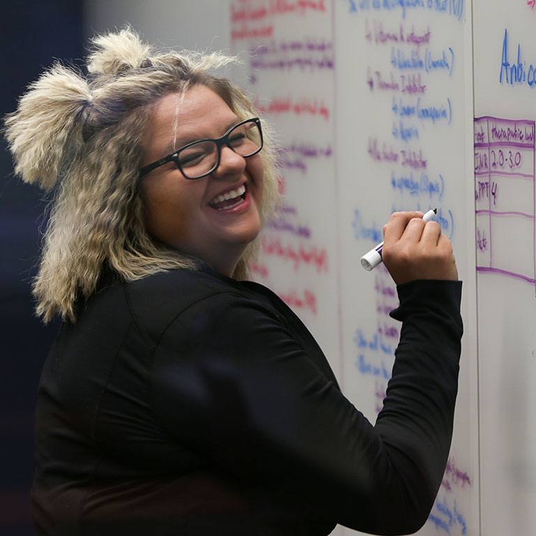 Student smiling and writing on a board.