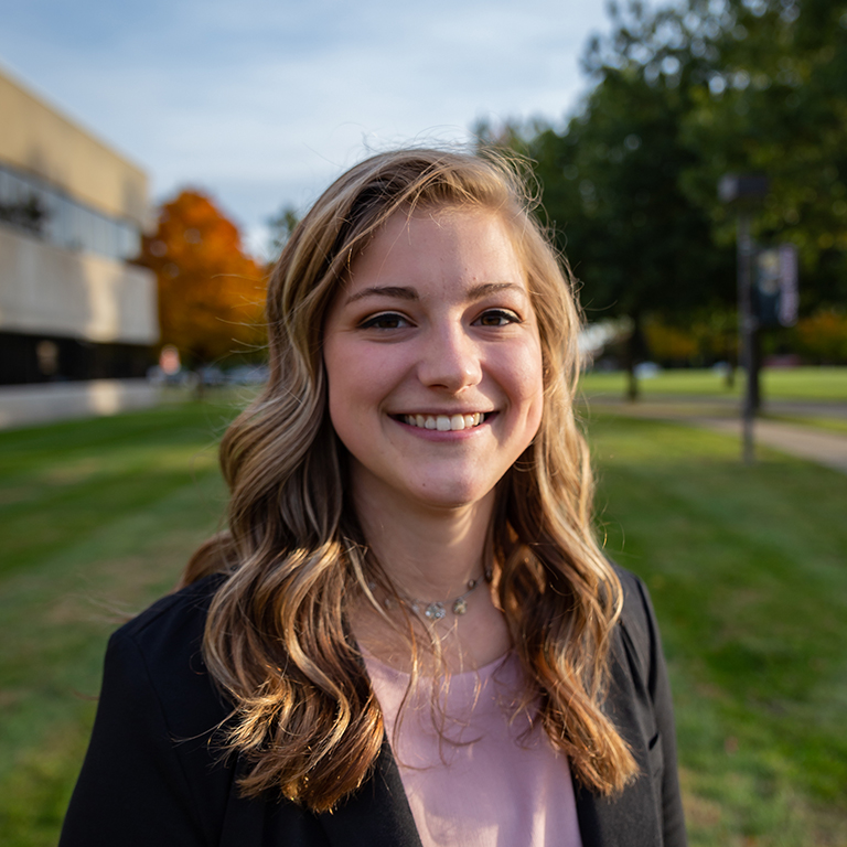 Student smiling, standing outside a campus building.
