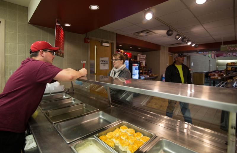 A cafe staff helping a student order food by a counter.