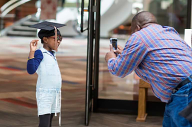 A man taking a photo of a child in a graduation cap.